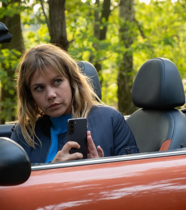 „Neuer Wind im Alten Land – Beke wirbelt auf“: Beke (Felicitas Woll) sitzt in ihrem offenen Cabrio und macht aus dem Auto heraus ein Bild mit ihrem Handy.