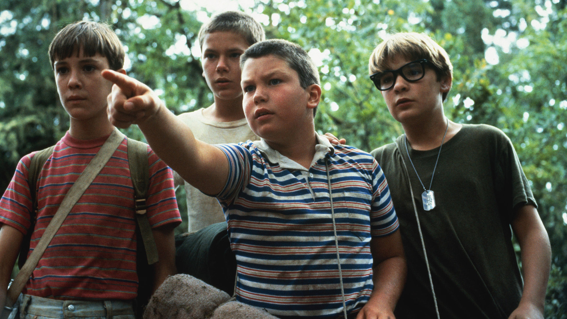"Stand by Me - Das Geheimnis eines Sommers": Gordie (Wil Wheaton), Chris (River Phoenix), Teddy (Corey Feldman) und Vern (Jerry O´Connell) stehen nebeneinander im Wald und schauen aufmerksam in die Ferne, während Vern auf etwas zeigt.