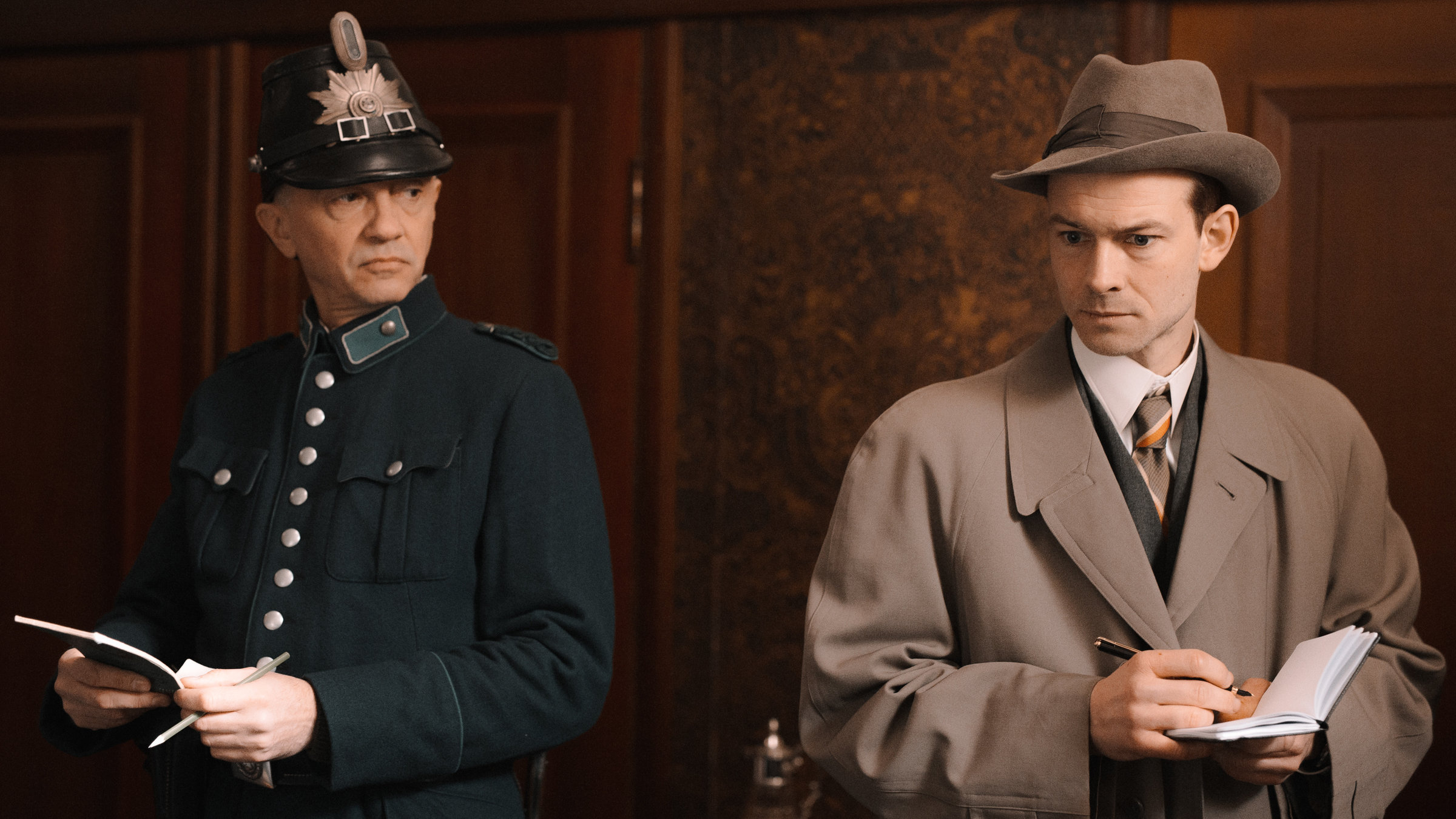 "Terra X: Ein Tag in Berlin 1926": Der Schutzpolizist (Dzintars Krumiņs) und Kriminalkommissar Fritz Kiehl (Christian Clauß) stehen nebeneinander und machen sich Notizen.