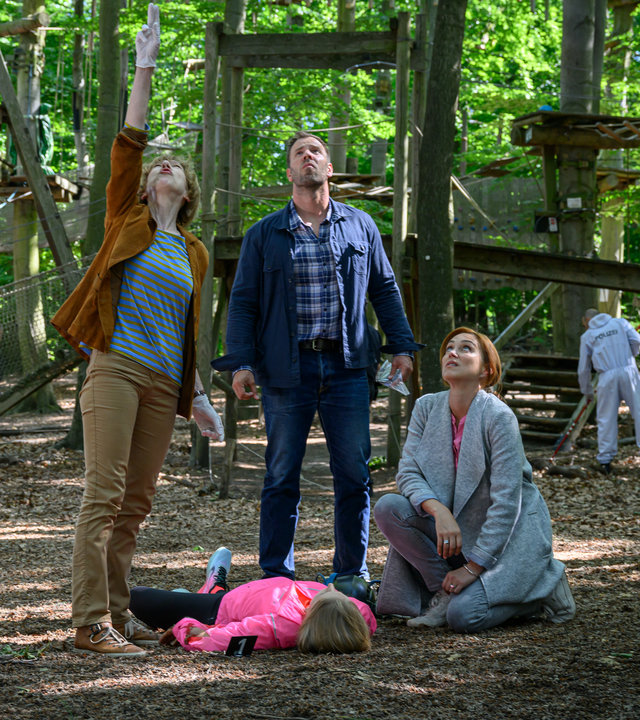 "SOKO Wismar – Tiefer Fall": Das Opfer Antje Kölling (Kim Ruhnau) liegt im Kletterpark im Wald auf dem Boden. Das Ermittlungsteam, Dr. Helene Sturbeck (Katharina Blaschke), Lars Pöhlmann (Dominic Boeer) und Karoline Joost (Nike Fuhrmann) stehen um das Opfer herum und blicken nach oben zur Absturzstelle.