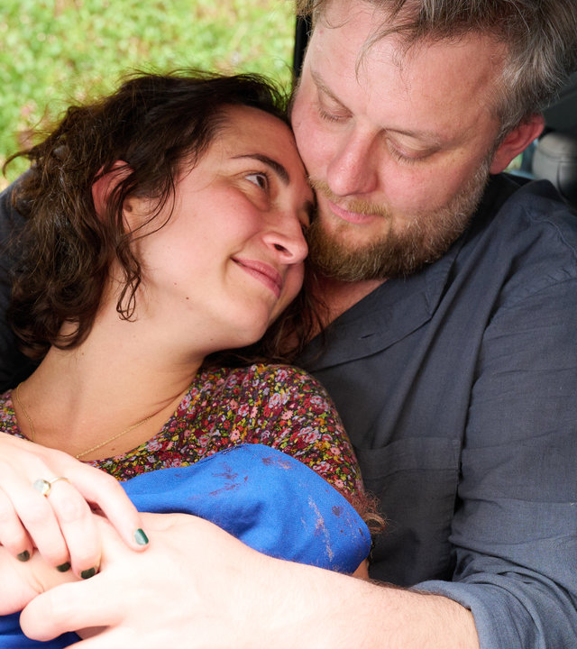 "Aufgestaut - Greta": Zeynep (Miriam Ohlmeyer) hält ihr Baby in den Armen, das in ein blaues Tuch gewickelt ist, und lehnt sich an Max (Fatoni) an, der hinter ihr sitzt und sie in den Armen hält.