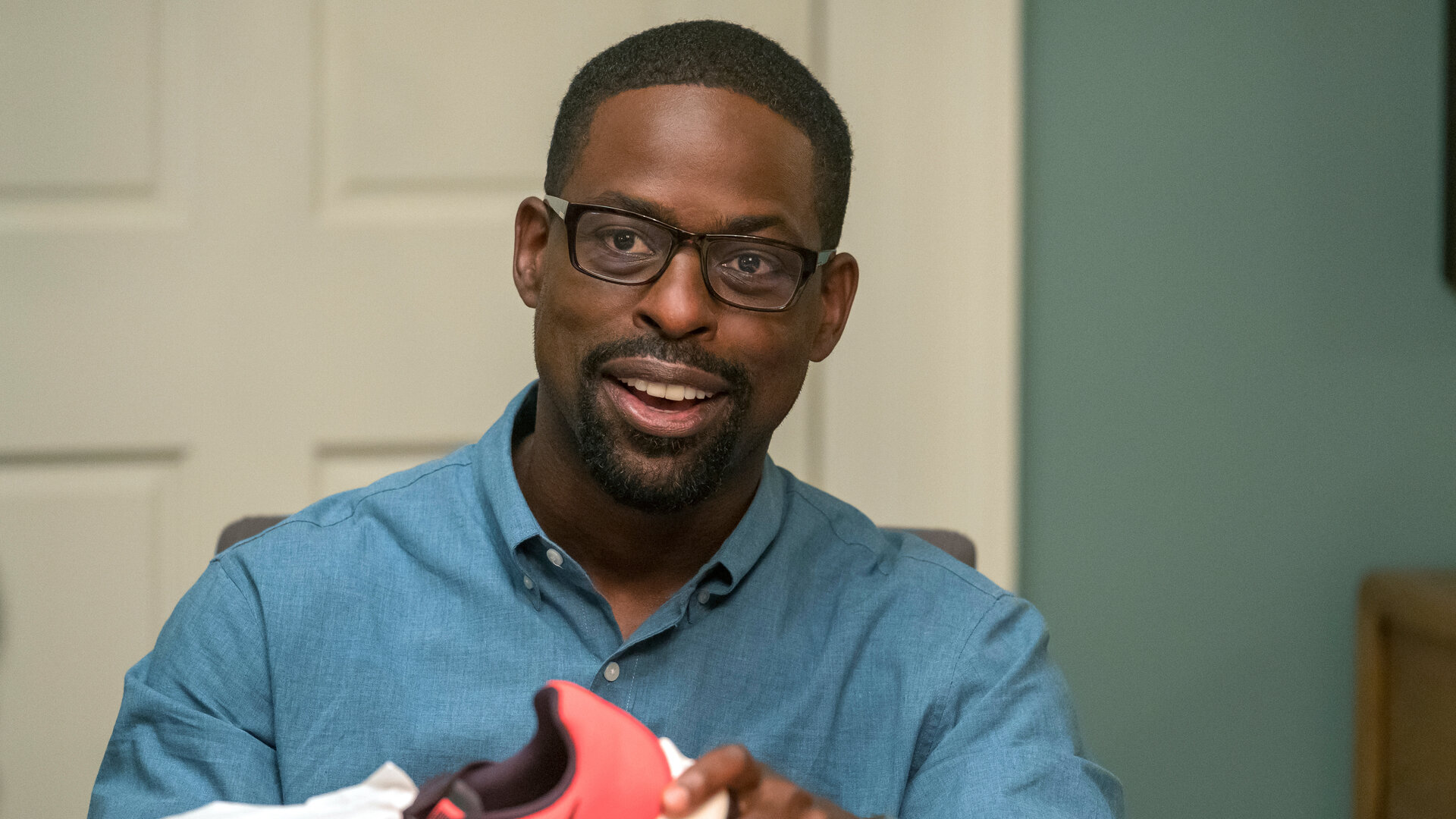 "This Is Us - Das ist Leben: Neun Dollar": Randall Pearson (Sterling K. Brown) sitzt an einem Tisch und packt Turnschuhe aus einem Schuhkarton aus. Er blickt lächelnd nach vorn.