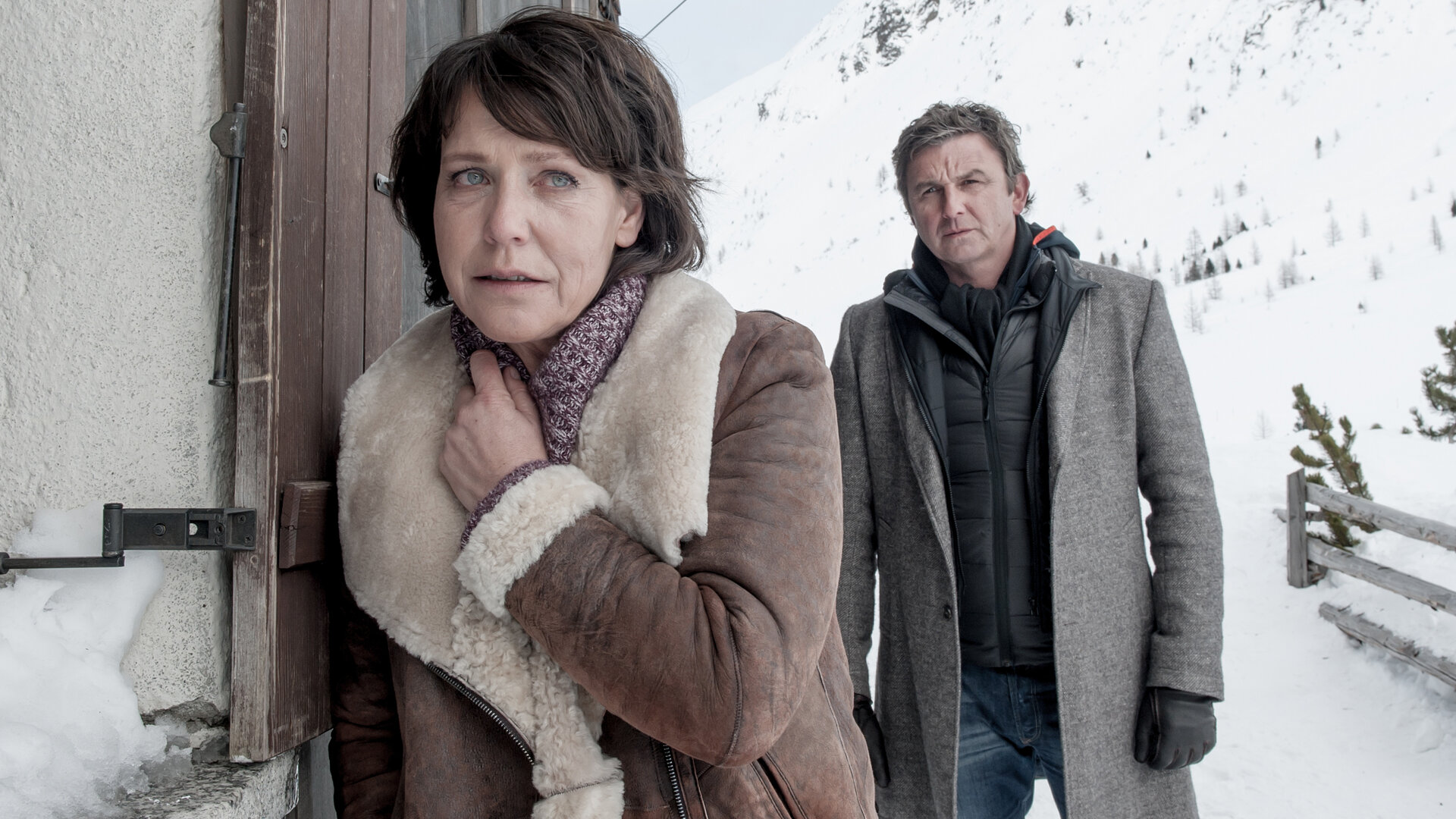 "Der Bergdoktor - Gestohlenes Glück": Sabine Moser (Janina Hartwig) steht an der Hauswand im Schnee und lehnt sich an einen Fensterladen. Hinter ihr steht Dr. Martin Gruber (Hans Sigl) und sieht sie an.
