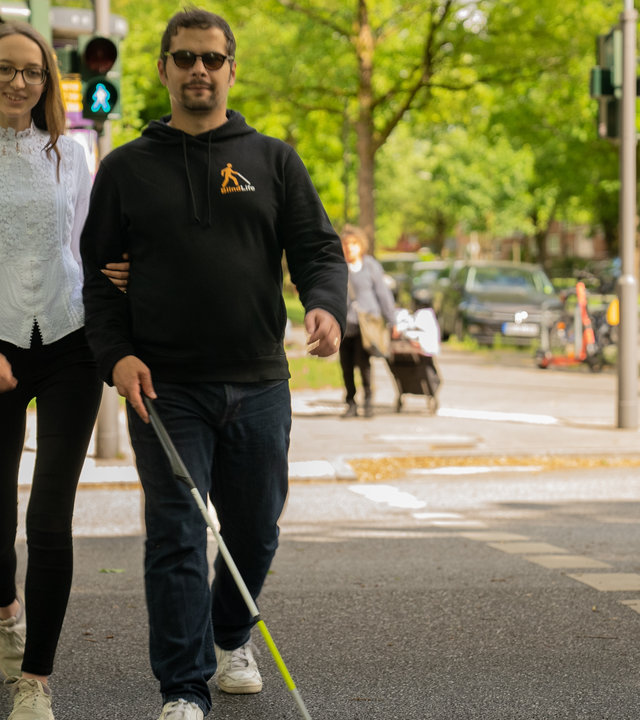 "einfach Mensch : Erdin und Jasmin - Mr. and Mrs. Blindf Life": Erdin und Jasmin, das blinde Pärchen, geht eine Straße entlang.