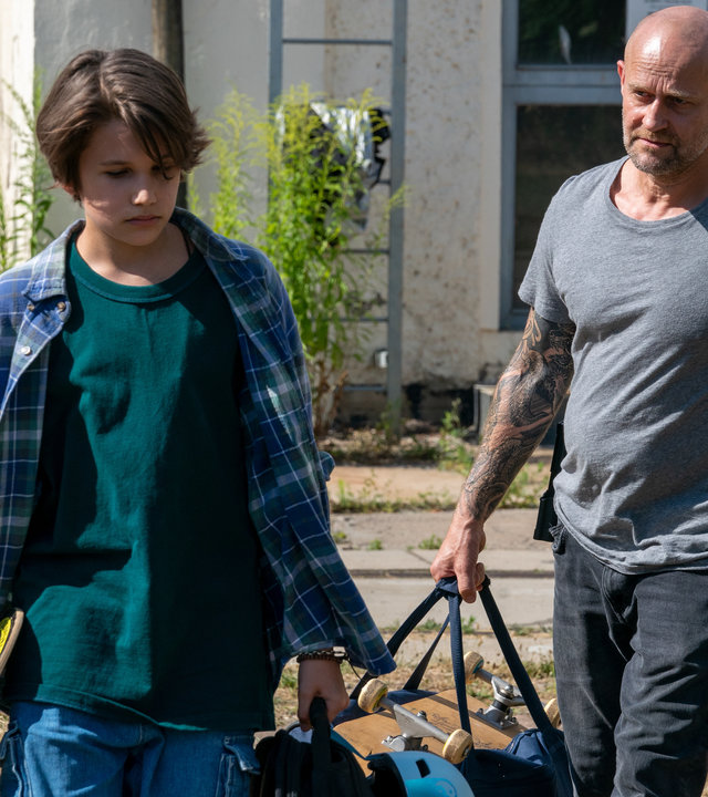 "Jenseits der Spree - Tommy": Tommy (Linus Kranich) und Robert (Jürgen Vogel) tragen Skateboards und Taschen, während sie über ein Gelände laufen. Robert geht knapp hinter Tommy und schaut ihn dabei fragend an.