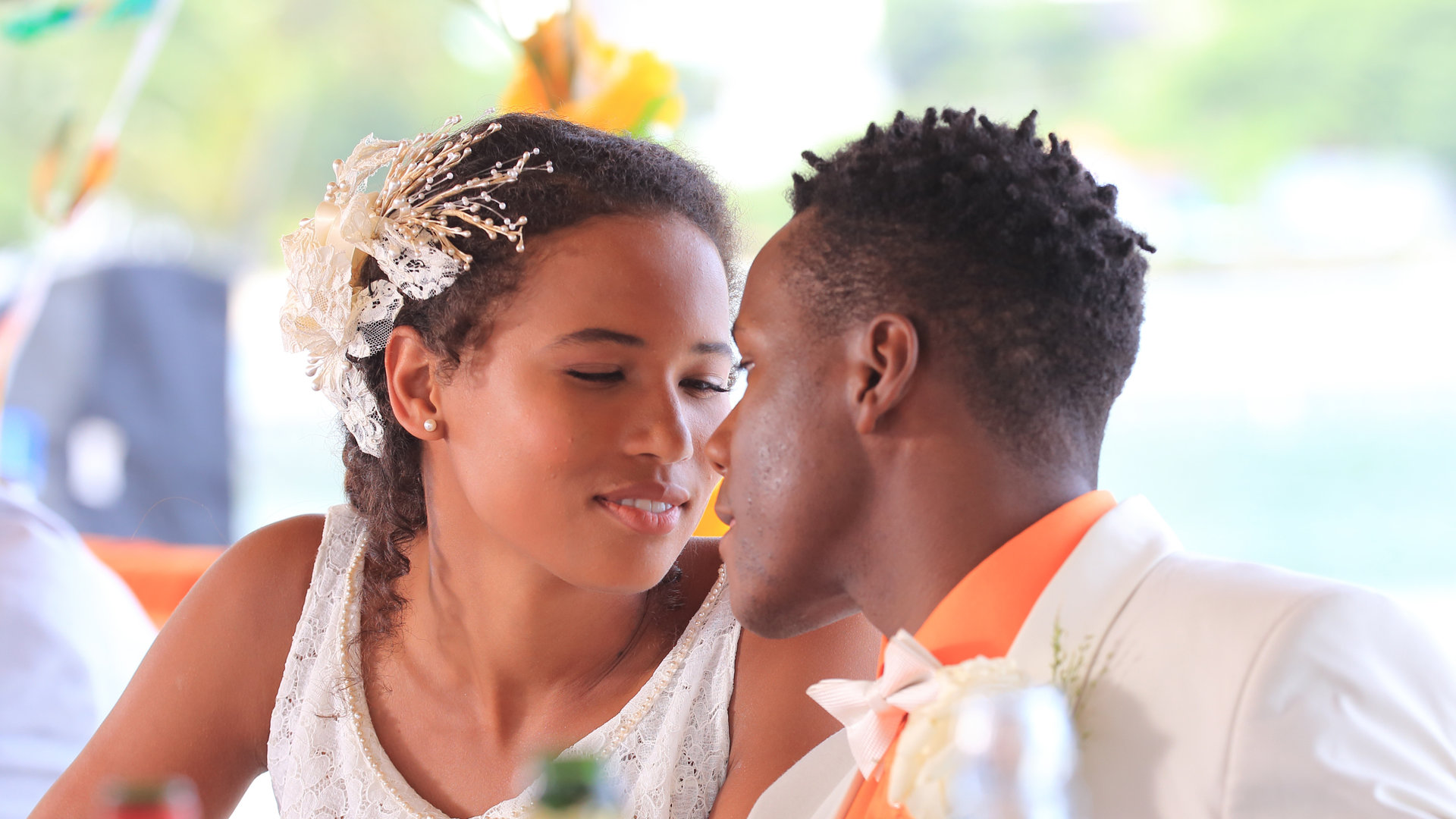 "Death in Paradise - Von Liebe und Tod": Rosey (Fola Evans-Akingbola) und J.P. (Tobi Bakare) haben gerade geheiratet, sitzen am Tisch und schauen sich tief in die Augen.