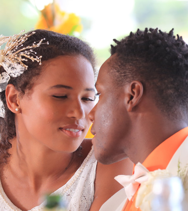 "Death in Paradise - Von Liebe und Tod": Rosey (Fola Evans-Akingbola) und J.P. (Tobi Bakare) haben gerade geheiratet, sitzen am Tisch und schauen sich tief in die Augen.