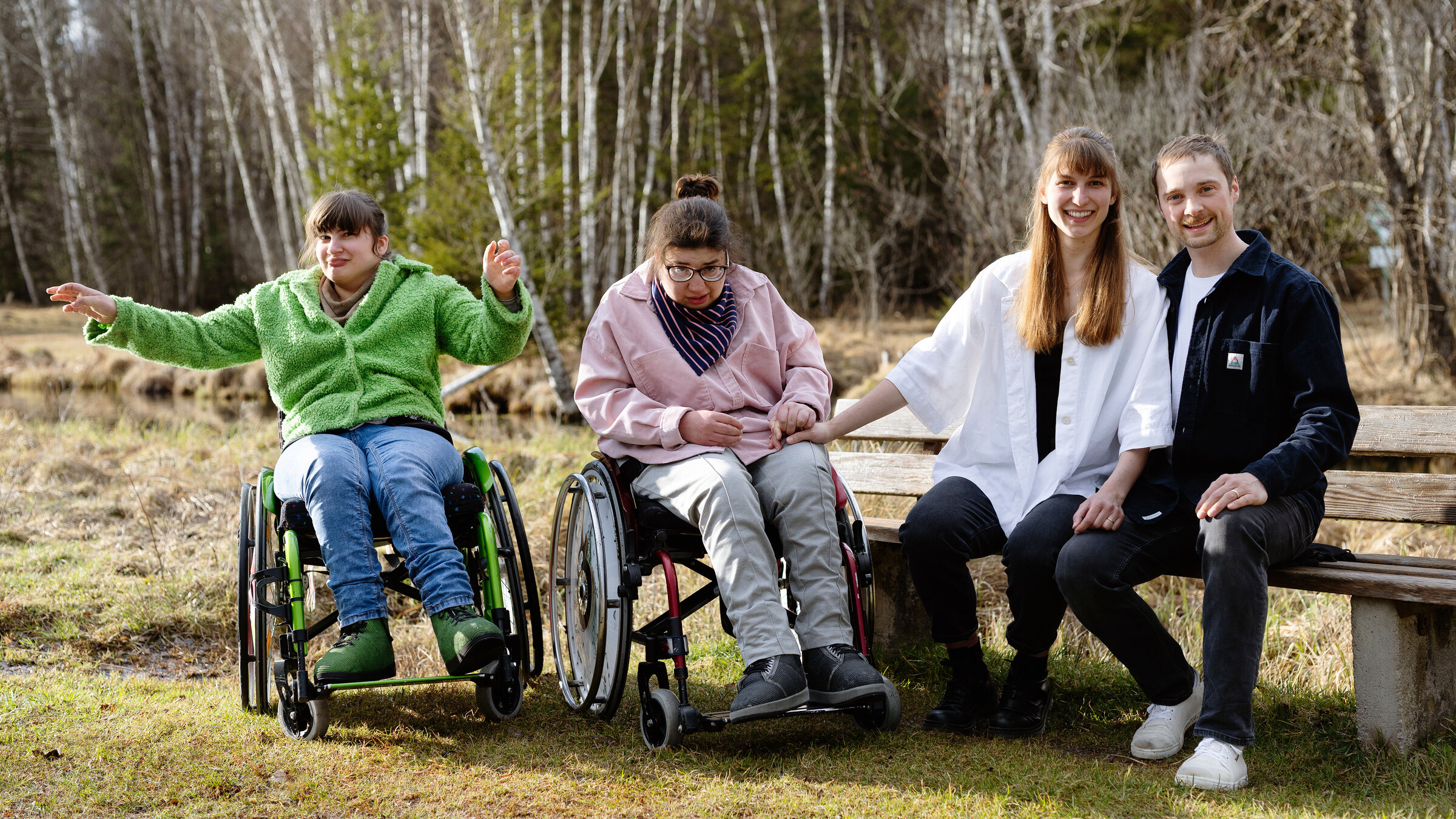 "37°Leben: Hält meine Beziehung das aus? Nicht ohne meine Geschwister": Janika und Bene sitzen auf einer Bank im Freien, neben ihnen in ihren Rollstühlen Sarah und Lea. Sie befinden sich in der Natur, um die Bank herum ist eine Wiese, dahinter liegt ein Birkenwald.