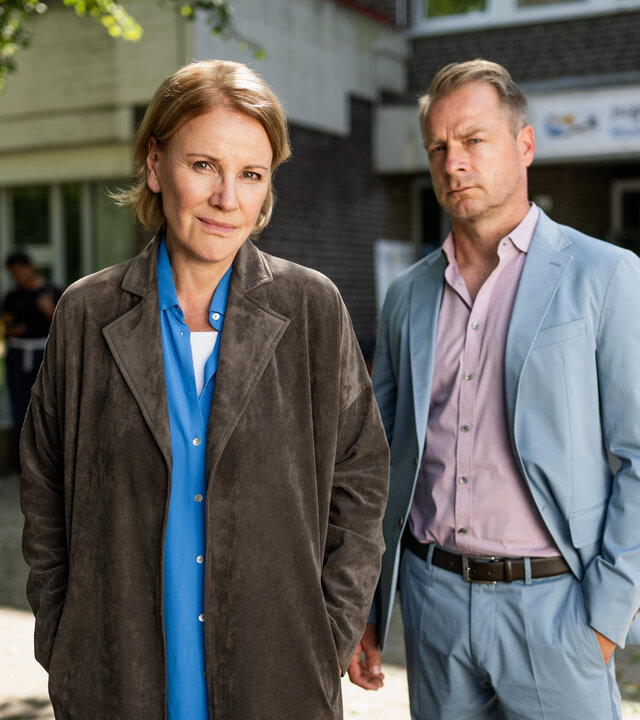 "Marie Brand und die verlorenen Kinder": Marie Brand (Mariele Millowitsch) steht zusammen mit Jürgen Simmel (Hinnerk Schönemann) vor dem Eingang eines Kinderhorts. Im Hintergrund stehen mehrere Jugendliche (Komparsen) vor den Eingangstüren.