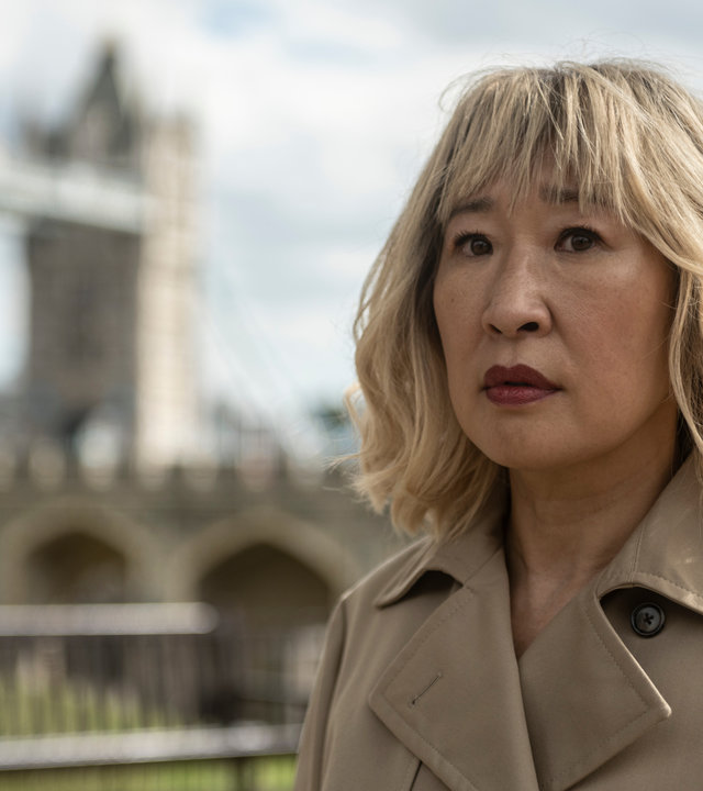 "Killing Eve - Nicht fressen lassen": Eve (Sandra Oh) steht draußen und schaut ernst zur Seite. Dabei trägt sie eine blonde Perücke und einen beigen Trenchcoat.