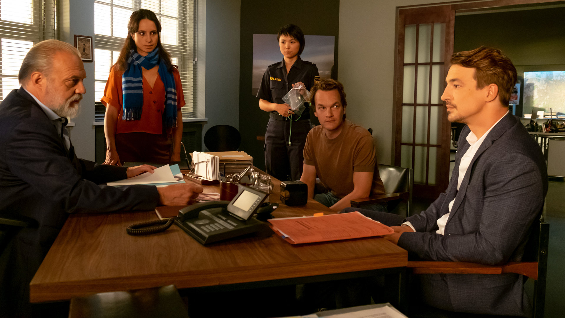"Der Alte - Zeugen der Anklage": Richard Voss (Jan-Gregor Kremp), Annabell Lorenz (Stephanie Stumph), Julia Lulu Zhao (Yun Huang), Tom Kupfer (Ludwig Blochberger) und Dr. Alexander Spohr (Sebastian Fischer) haben sich rund um Voss'' Schreibtisch versammelt. Alle hören Staatsanwalt Dr. Alexander Spohr gespannt zu.
