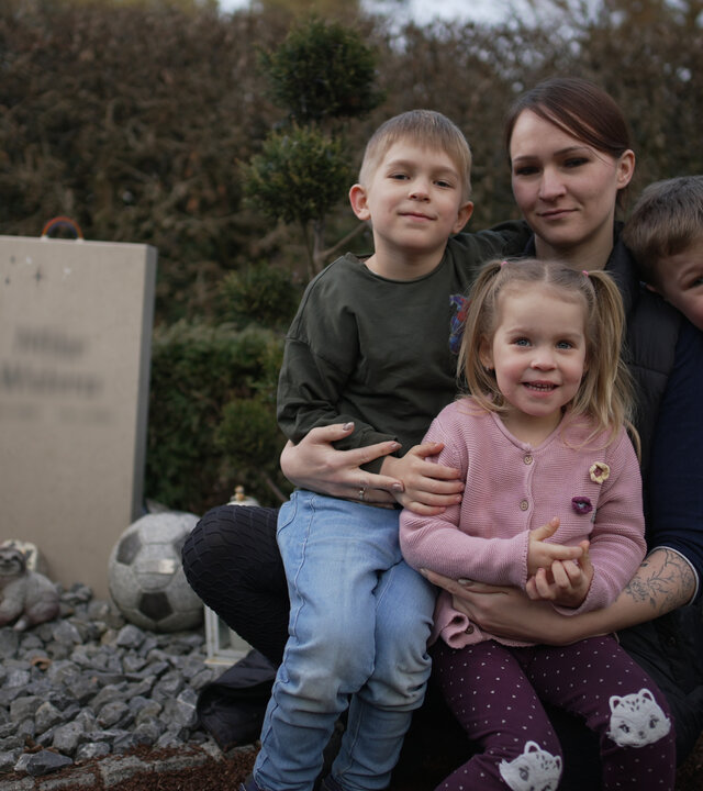 "37°Leben: Aus dem Leben gerissen": Johanna (29) sitzt neben einem Grab. Zwei ihrer Kinder sitzen auf ihren Beinen. Ein kleiner Junge steht in gebeugter Haltung rechts neben ihr, sein Kopf liegt auf ihrer linken Schulter.