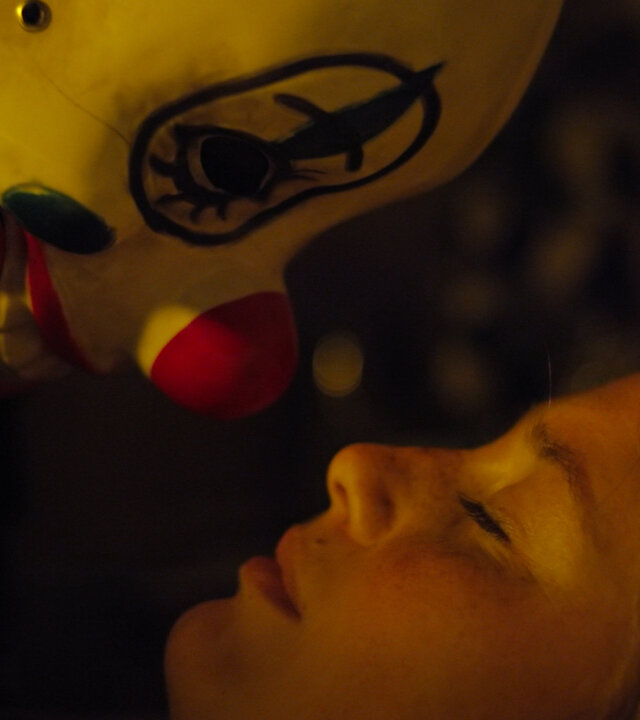 "Notruf Hafenkante - Besuch in der Nacht": Großaufnahme: Der Kopf der schlafenden Mina (Bianca Nawrath) liegt auf dem Bett, nah über ihrem Kopf ist der Kopf eines Mannes, der eine Clownsmaske trägt. Es schaut sie an.