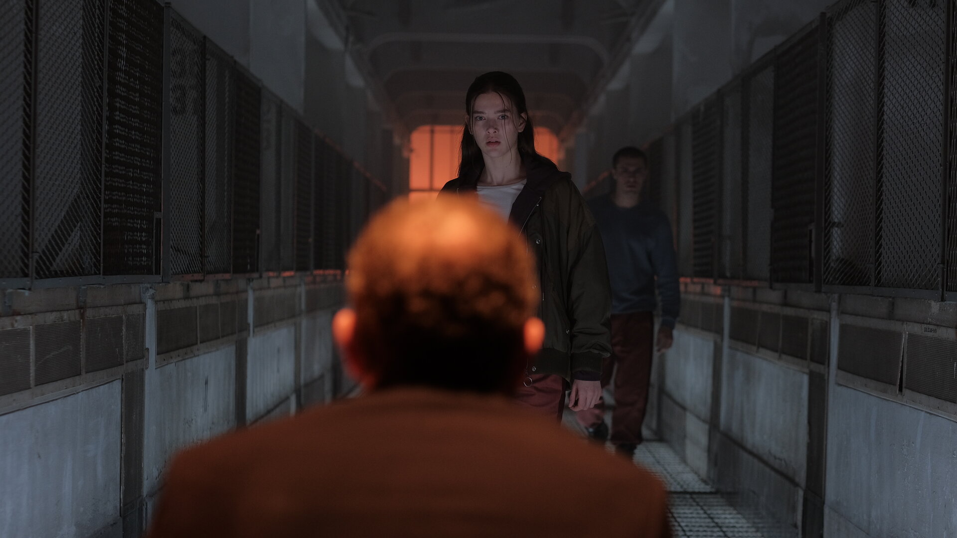 "Fallen - Ausgeflogen": Luce (Jessica Alexander) steht dem Outcast (Rod Hill) mit ernstem Blick gegenüber. Hinter ihr steht Daniel (Gijs Blom) in einem düsteren Gang mit Gitterwänden zu beiden Seiten.