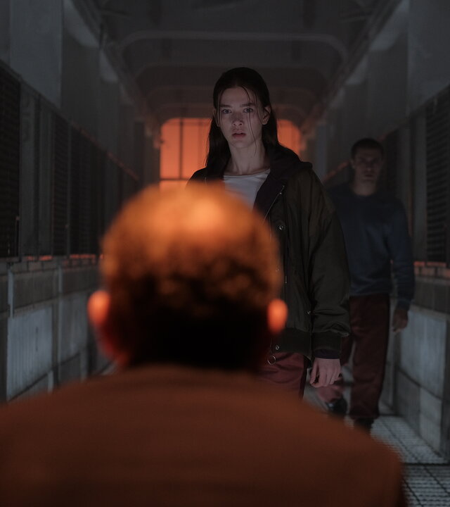 "Fallen - Ausgeflogen": Luce (Jessica Alexander) steht dem Outcast (Rod Hill) mit ernstem Blick gegenüber. Hinter ihr steht Daniel (Gijs Blom) in einem düsteren Gang mit Gitterwänden zu beiden Seiten.