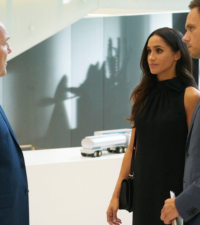 "Suits - Zerwürfnis": Die in schwarz gekleidete Rachel (Meghan Markle) und Mike (Patrick J. Adams), der in seinen Händen ein Dokument hält,  hören konzentriert Larry Burnham (Larry Day) zu, der ihnen gegenübersteht.