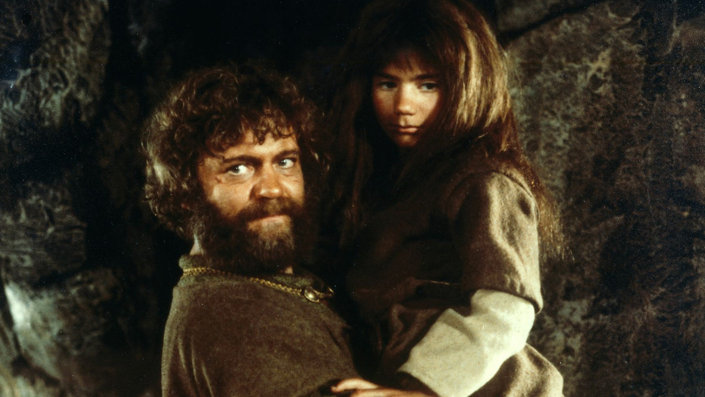 "Ronja, die Räubertocher": Mattis (Börje Ahlstedt) trägt Ronja in einer Höhle (Hanna Zetterberg) auf seinen Armen. Beide schauen in verschiedene Richtungen.