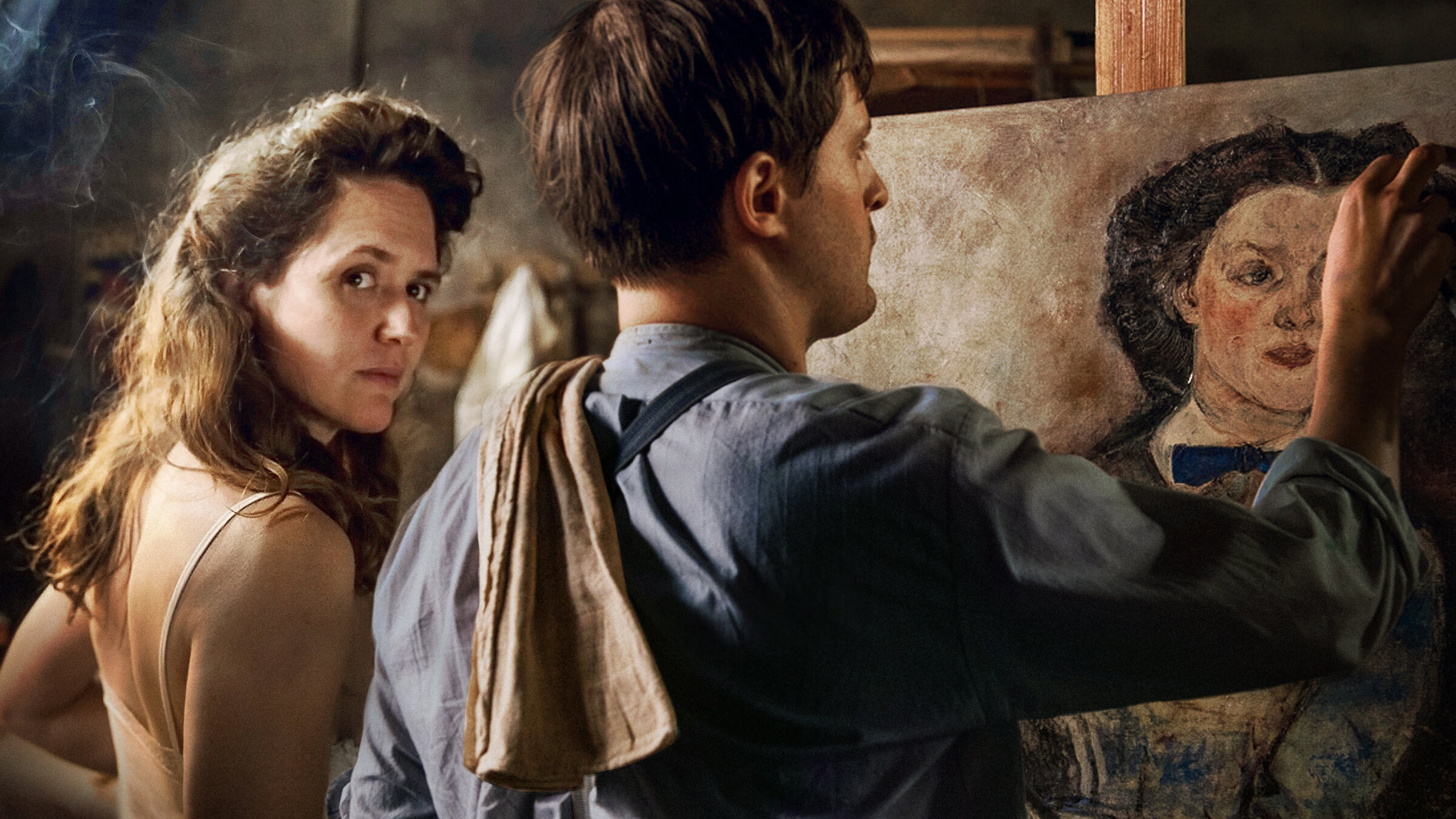 "Alma & Oscar": Alma Mahler (Emily Cox) und Oskar Kokoschka (Valentin Postlmayr) stehen vor einem Gemälde, das auf einer Staffelei steht. Während er daran arbeitet, schaut sie, nur mit einem Unterhemd bekleidet, über die Schulter in die Kamera.