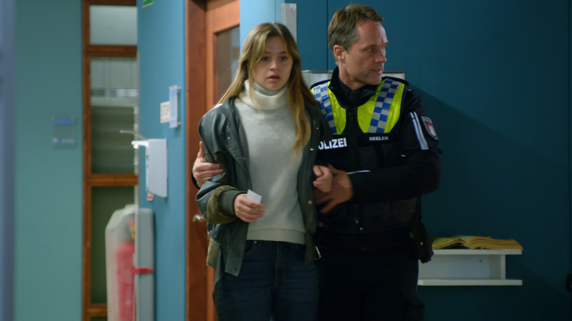 "Notruf Hafenkante - Gefährliche Mission": Der Polizist Mattes Seeler (Matthias Schloo) geht mit Michelle (Flora Li Thiemann) über den Gang des Elbkrankenhauses. Er hat seinen rechten Arm um Michelle gelegt und stützt sie. Michelle schaut entsetzt.