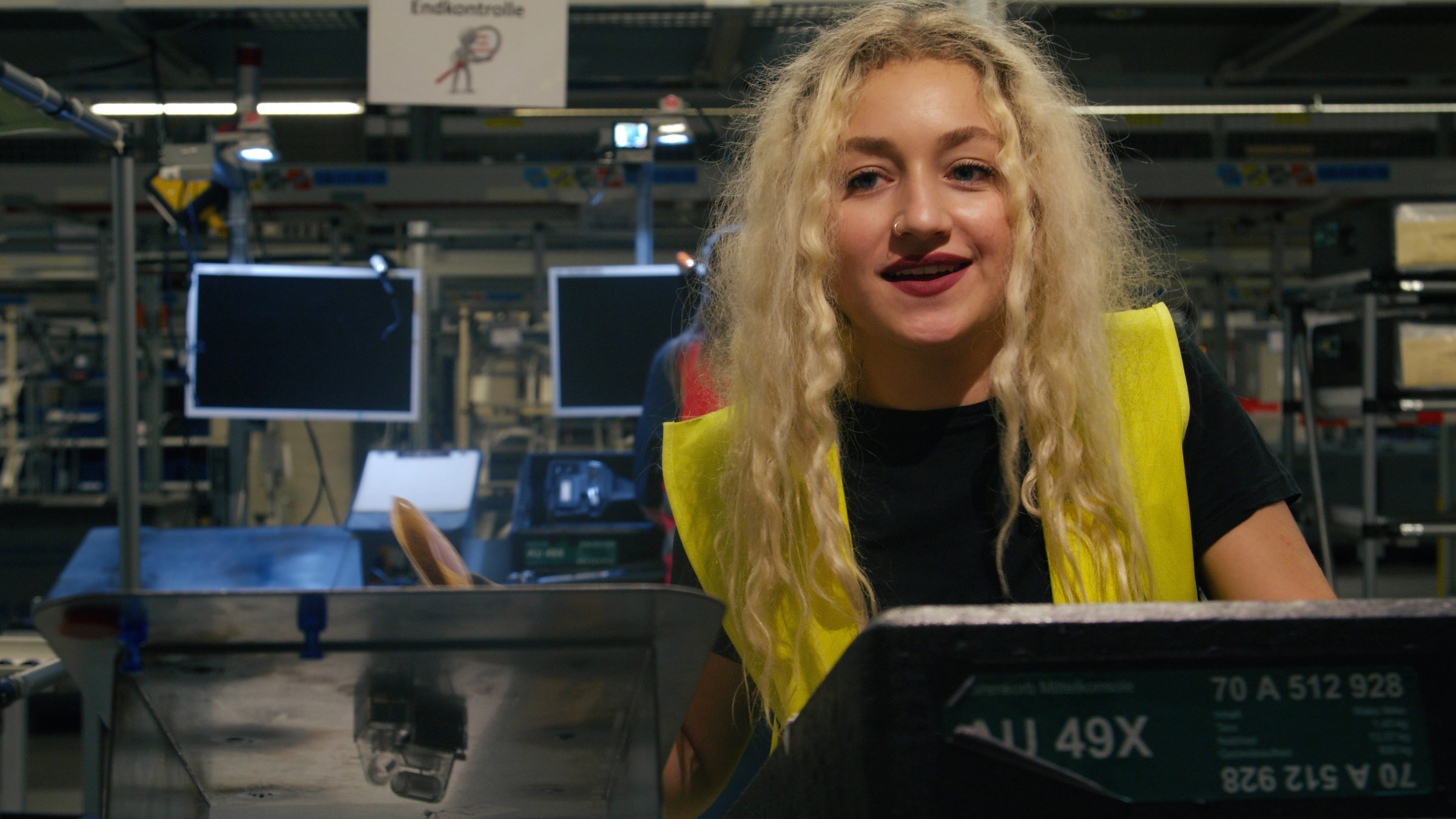 "Ab 18! - Seda baut Autos": Nahaufnahme von blondem Mädchen, das an einem Schalter steht und lacht.