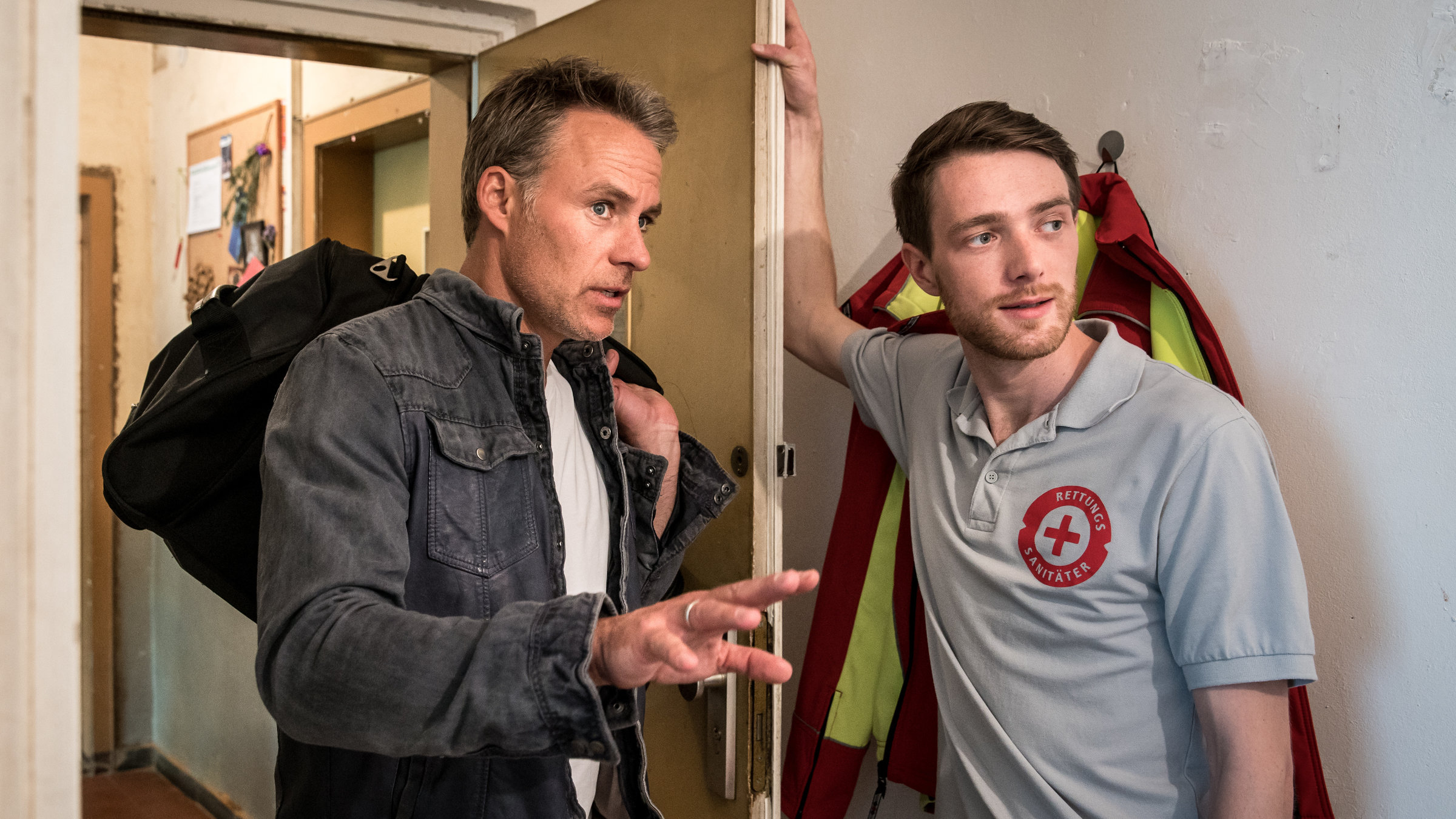 "SOKO Leipzig - Not OP": Jan Maybach (Marco Girnth) geht durch die T&uuml;r zu Benny Maybachs (Maximilian Klas) Wohung. Benny Maybach steht angelehnt an der ge&ouml;ffneten T&uuml;r.