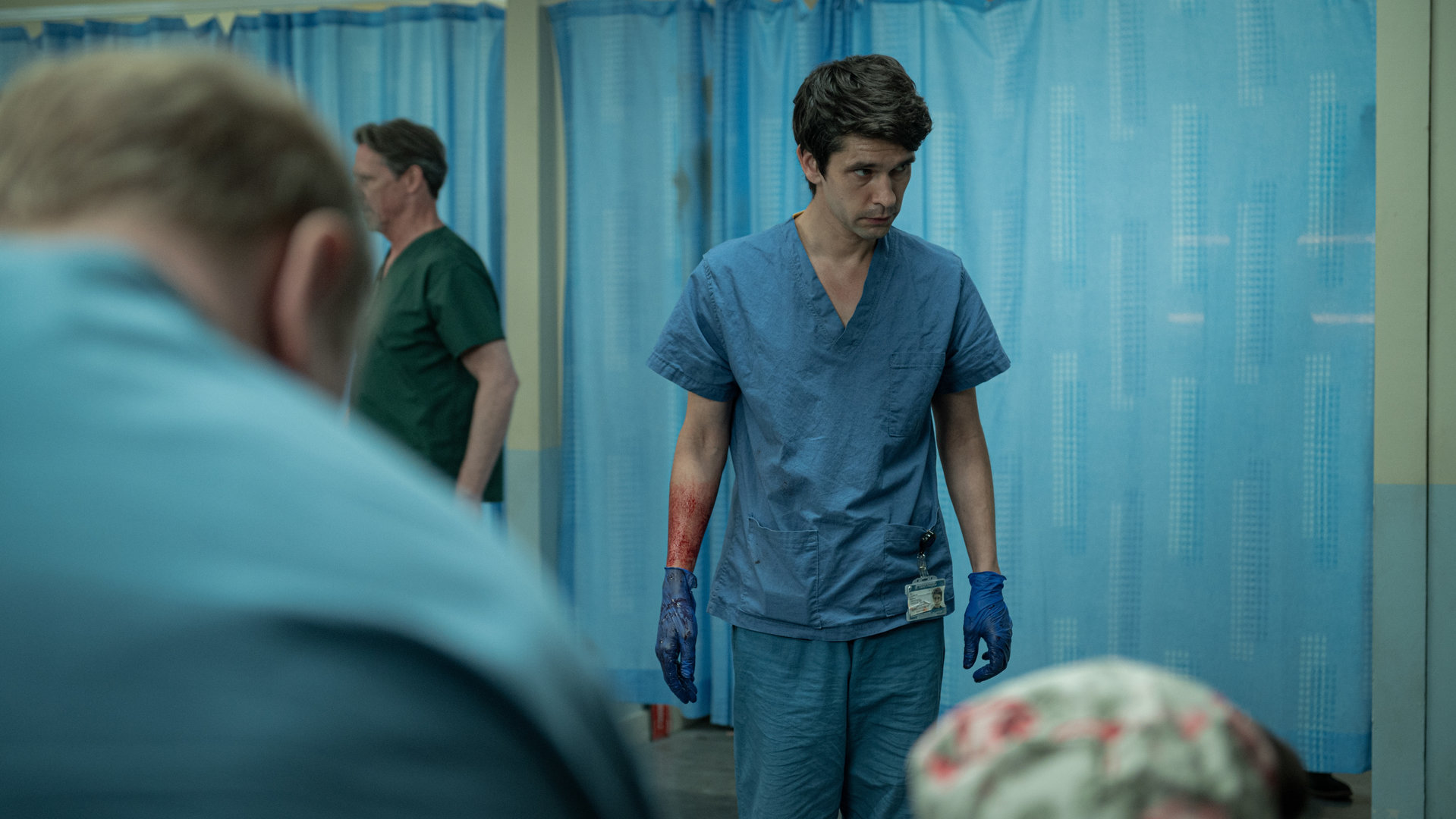 "This Is Going To Hurt - Glück im Unglück": Adam (Ben Whishaw) steht im Gang einer Krankenstation und schaut besorgt auf den Boden. Dabei trägt er seine Arztklamotten und hat Gummihandschuhe übergezogen.
