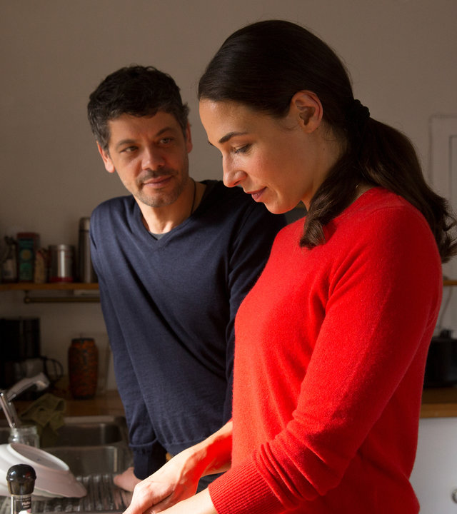 "SAFE - Episode 2": Katinka (Judith Bohle) und Tom (Carlo Ljubek) stehen nebeneinander vor einer Küchenzeile und reden. Katinka schneidet Gemüse. Auf der Küchenzeile sind diverse Tassen, Teller und andere Küchenutensilien zu sehen. Im Hintergrund sind eine Tür und ein Tisch zu sehen.