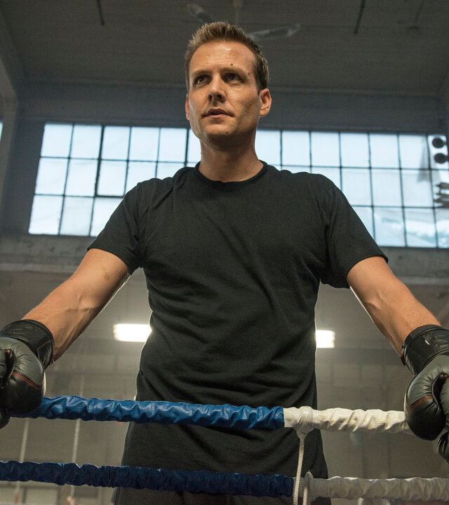 "Suits - Überraschungsangriff": Harvey (Gabriel Macht) steht mit ernstem Blick und in schwarzem T-Shirt im Boxring. Er trägt Boxhandschuhe und stützt sich auf die Seilbegrenzung. Im Hintergrund sind die hohen Fenster der Trainingshalle zu sehen.