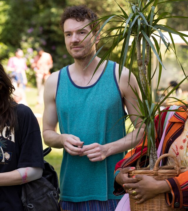 This Is Gonna Be Great - Höhepunkt": Hanna (Mona Vojacek Koper), David (Rein Mulder) und Aisha (Abigail Abraham) stehen nebeneinander im Grünen. Im Hintergrund befinden sich weitere Menschen. Hanna hantiert mit ihrem Handy. Aisha hält eine große Topfpflanze im Arm.
