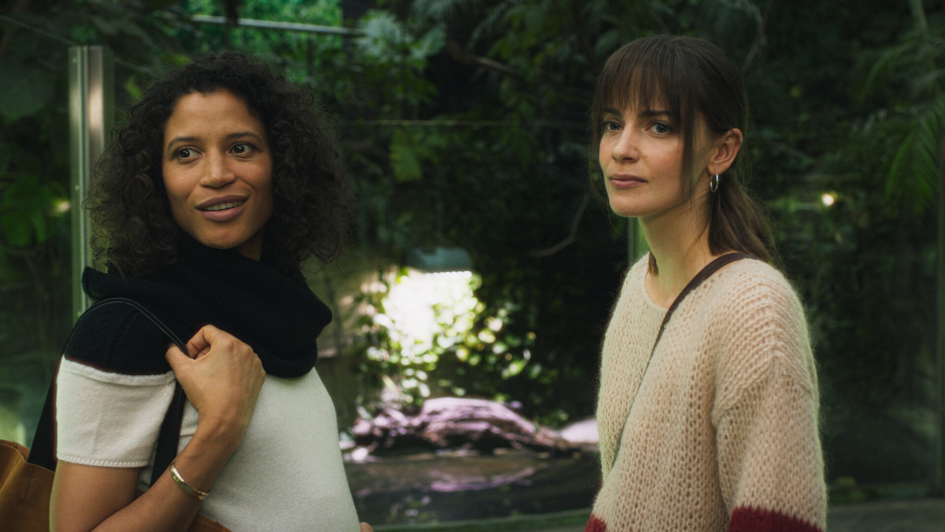 "Bauchgefühl - Zoe": Zoe (Davina Donaldson) und Lena (Laura Berlin) stehen im Zoo vor einem Terrarium und gucken gemeinsam auf etwas in der Ferne. Beide tragen Taschen über den Schultern. Zoe wirkt positiv, aber Lena verschlossen.