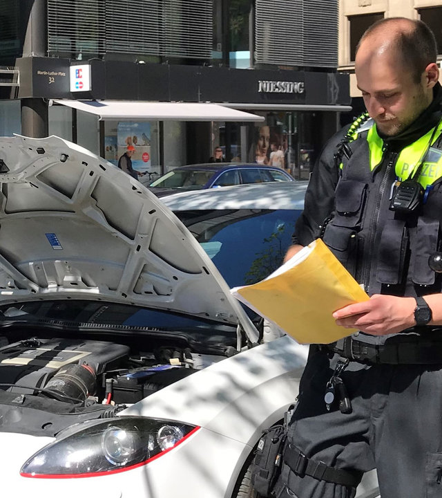 "Terra Xpress: Autoposer und Raser-Wahnsinn": Ein Mann steht vor der geöffneten Motorhaube seines Autos. Ein Polizist mit einer Mappe in der Hand steht neben dem Auto.