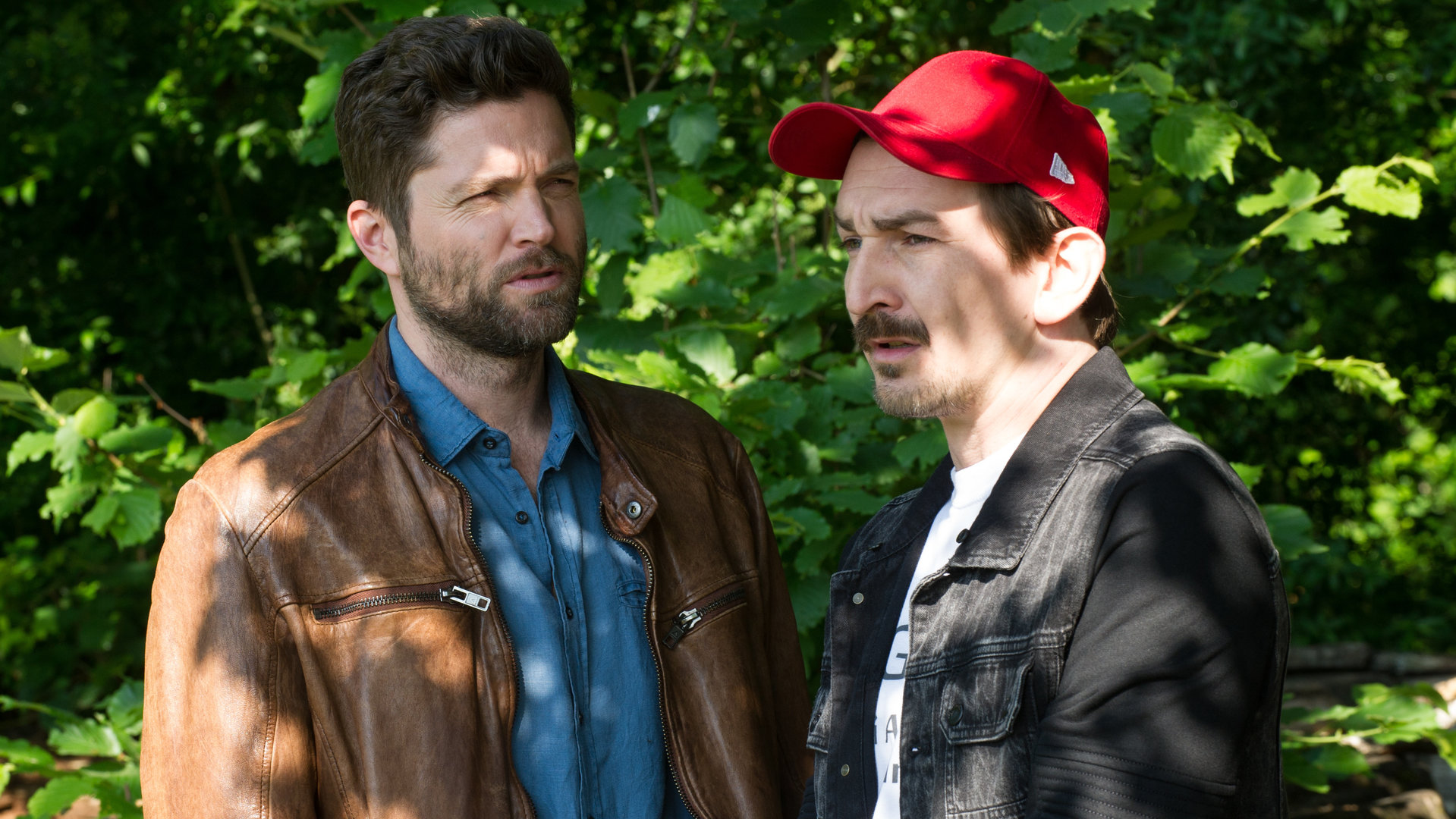 "SOKO Stuttgart - Cool bleiben": Jo Stoll (Peter Ketnath) und Bertram Fuchs (Till Wonka) sprechen miteinander. Sie stehen vor einem Gebüsch und sehen in unterschiedliche Richtungen.