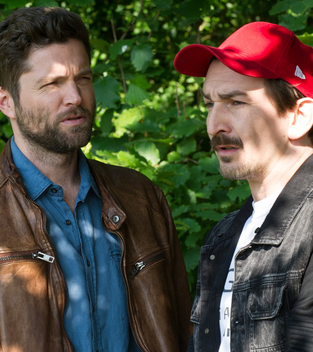 "SOKO Stuttgart - Cool bleiben": Jo Stoll (Peter Ketnath) und Bertram Fuchs (Till Wonka) sprechen miteinander. Sie stehen vor einem Gebüsch und sehen in unterschiedliche Richtungen.