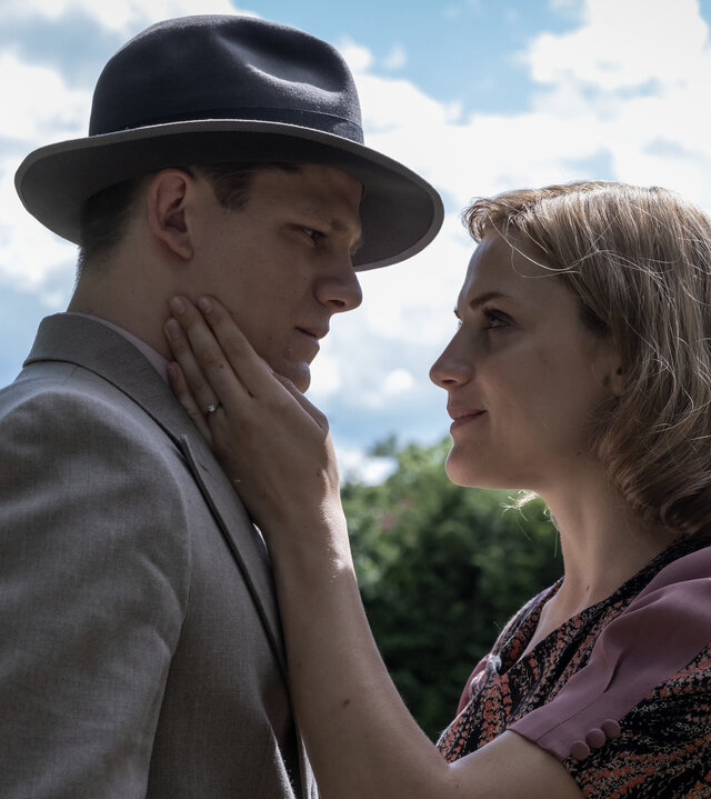 "Die Mittagsfrau": Helene (Mala Emde) steht mit Wilhelm (Max von der Groeben) auf einer Wiese und sie kommen sich näher. Im Hintergrund stehen Büsche vor einem Haus.