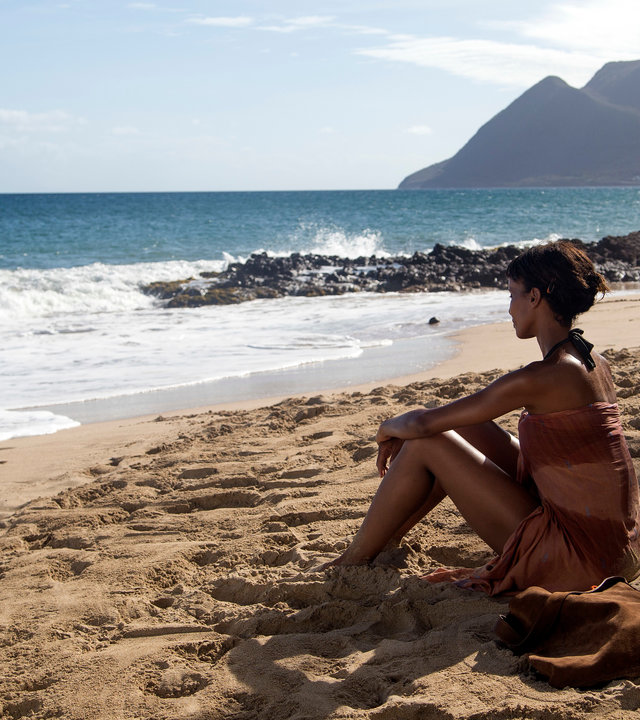 "Deadly Tropics - Götterdämmerung": Mélissa Sainte-Rose (Sonia Rolland) sitzt im Bikini am Strand und blickt auf das Meer.