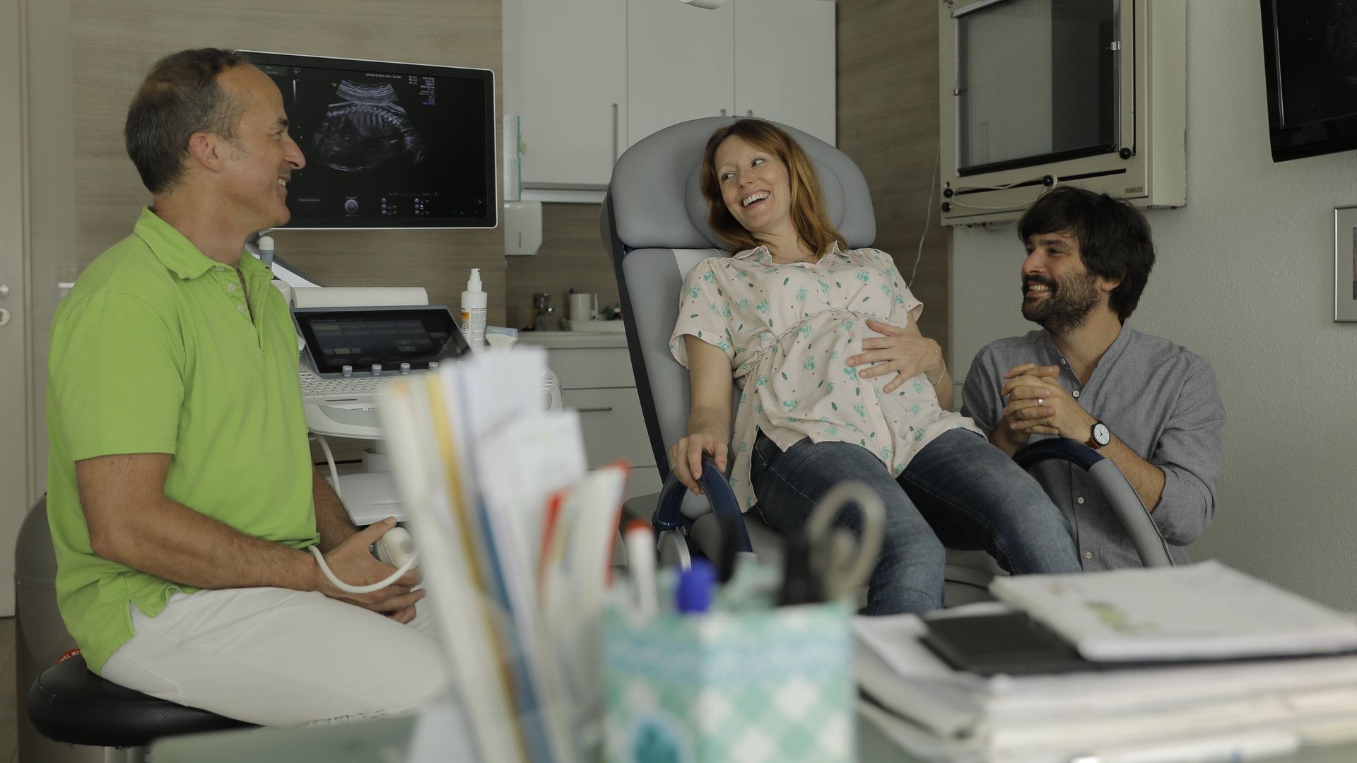 “Andere Eltern - Episode 5“: Im Behandlungszimmer lächeln Nina (Lavinia Wilson) und Jannos (Jasin Challah) den Gynäkologen erleichtert an.