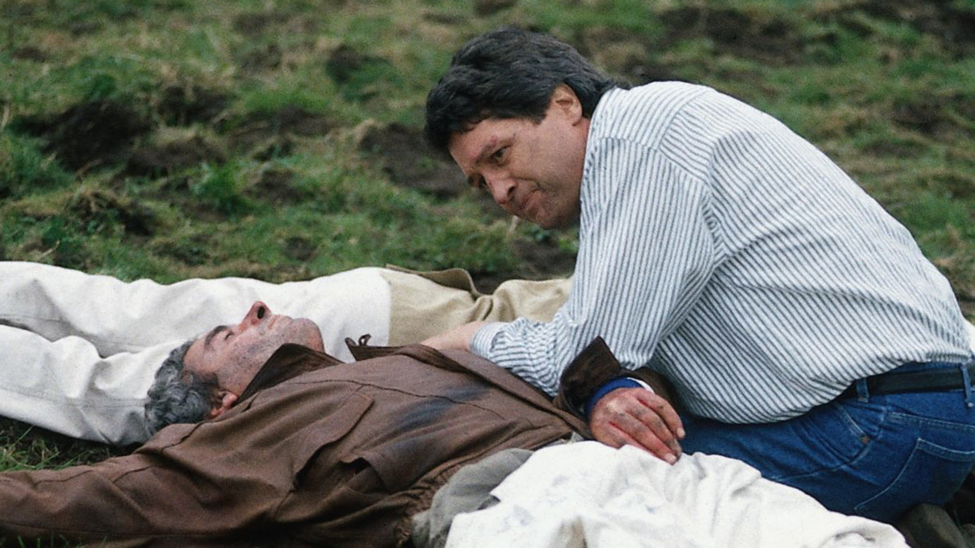 "Der Landarzt - Ein Kind wird vermisst": Dr. Mattiesen (Christian Quadflieg) kniet neben dem verletzten Piloten (Peter Hick) auf einer Wiese und versorgt ihn.