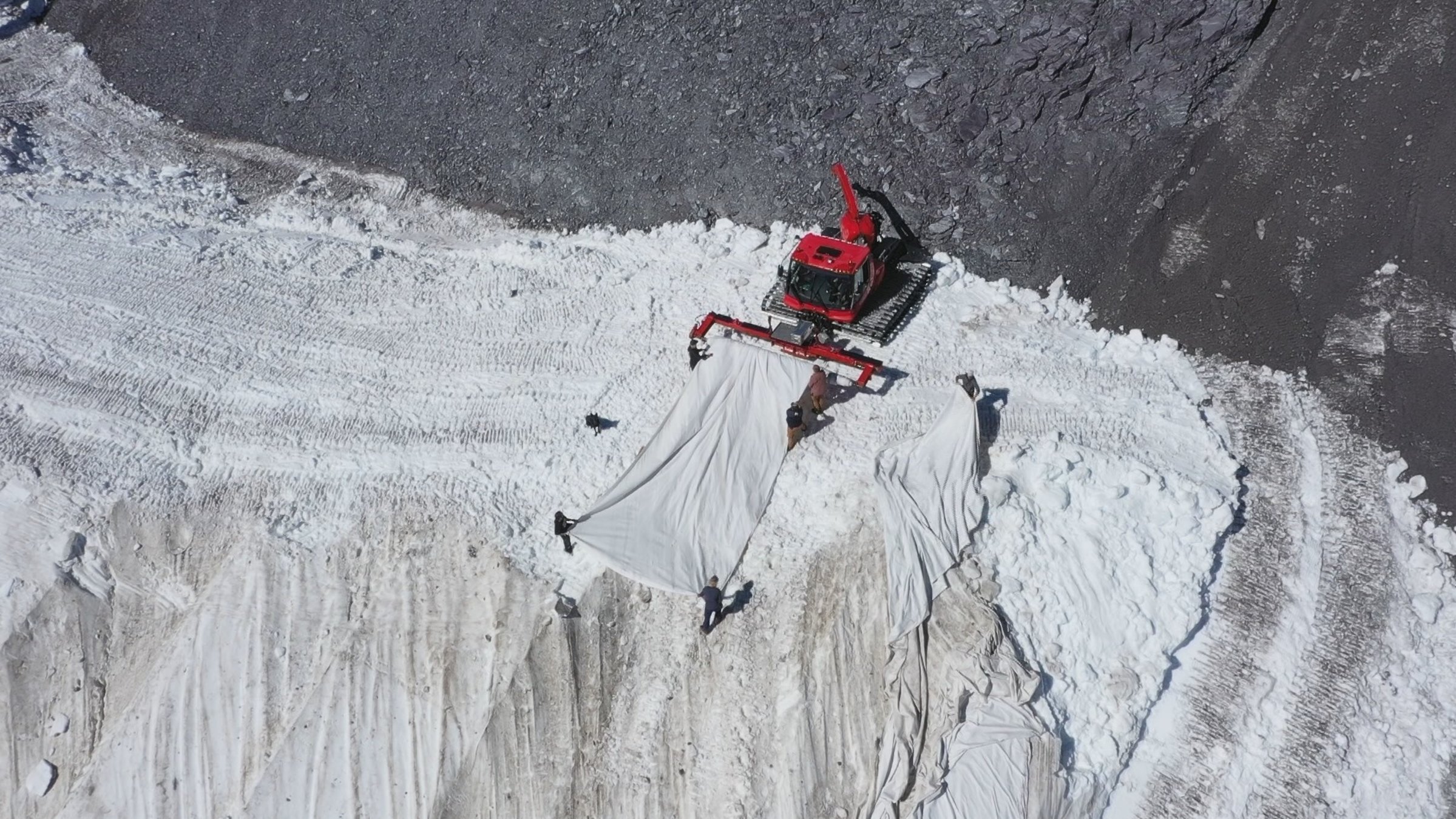 "SCHWEIZWEIT: Das Verschwinden des ewigen Eises": Von oben gesehen Mehrere Personen spannen mit Hilfe eines Raupenfahrzeugs eine weisses Tuch.