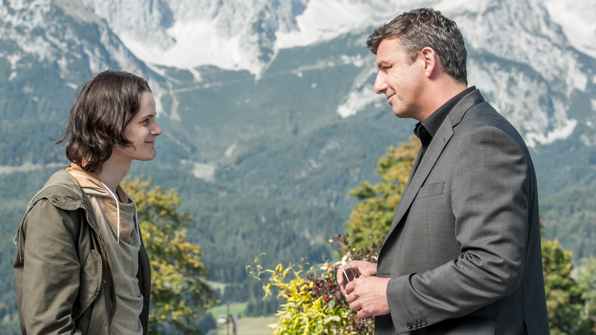 "Der Bergdoktor - Abschiede": Paul Ebert (Johannes Franke) und Martin Gruber (Hans Sigl) stehen sich lächelnd gegenüber. Im Hintergrund ist ein Bergpanorama zu sehen.