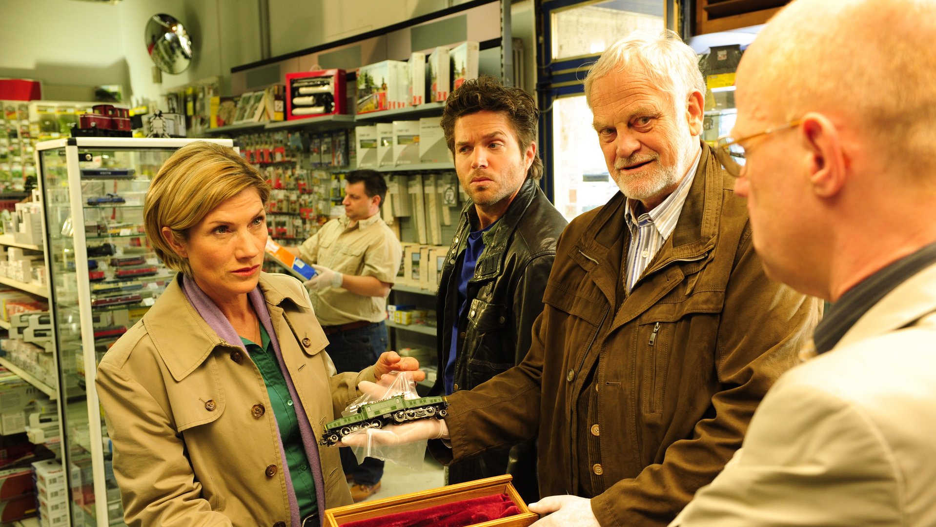 "SOKO Stuttgart - Krokodil": Martina Seiffert (Astrid M. Fünderich), Jo Stoll (Peter Ketnath), Friedemann Sonntag (Christian Paetzold) und Gerhard Wendt (Lutz Herkenrath) stehen zusammen in einem Laden und Friedemann Sonntag hält einen Gegenstand in der Hand. Im Hintergrund steht ein weiterer Spurensicherer.