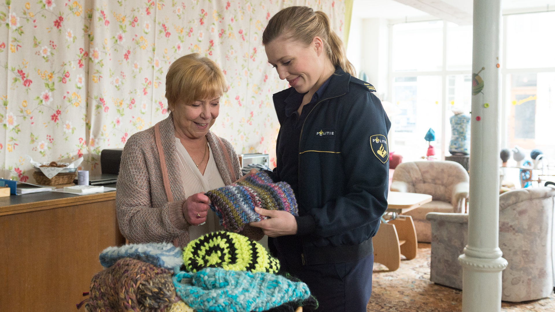 "SOKO Wismar – Lass das mal die Oma machen“: Anneke van der Meer (Isabel Berghout) und Cornelia Plank (Margot Rothweiler) stehen nebeneinander im gemütlichen Strickladen. Sie schauen sich interessiert bunte Strickmütze an, die vor ihnen in der Auslage liegen.