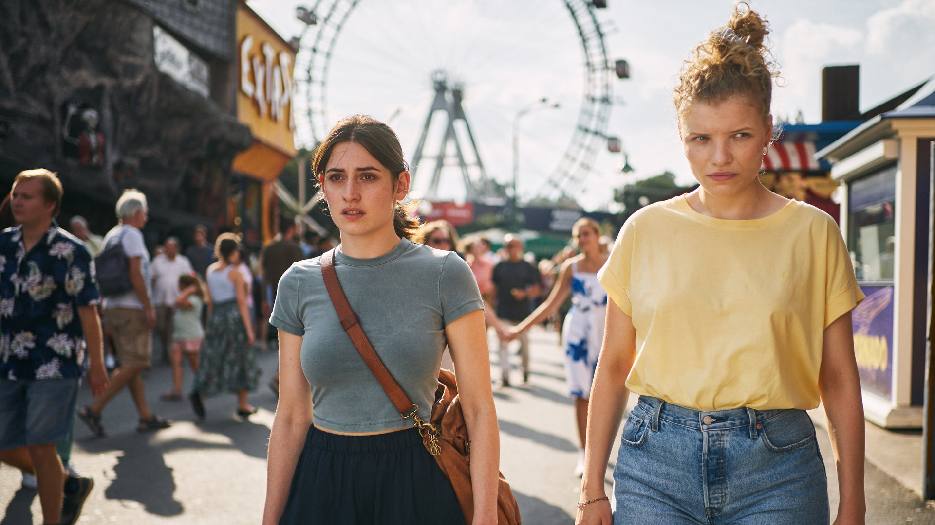 "Der Schatten - Schuld": Norah Richter (Deleila Piasko) und Theresa Winkler (Luisa-Céline Gaffron) laufen gemeinsam über den Wiener Prater. Sie schauen um sich. Im Hintergrund sind viele Menschen und das Wahrzeichen, das Riesenrad, zu sehen.