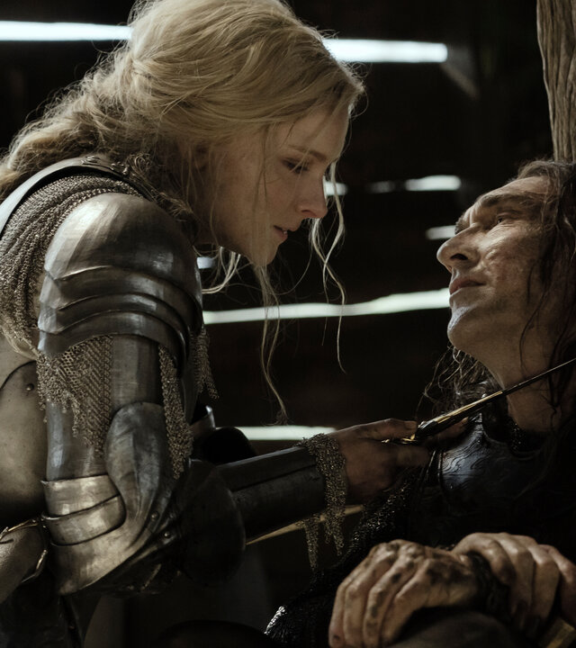 "Der Herr der Ringe: Die Ringe der Macht - Udun": Galadriel (Morfydd Clark) steht Adar (Joseph Mawle) in einer Scheune gegenüber. Sie trägt eine Rüstung und hält ihm einen Dolch an den Hals.