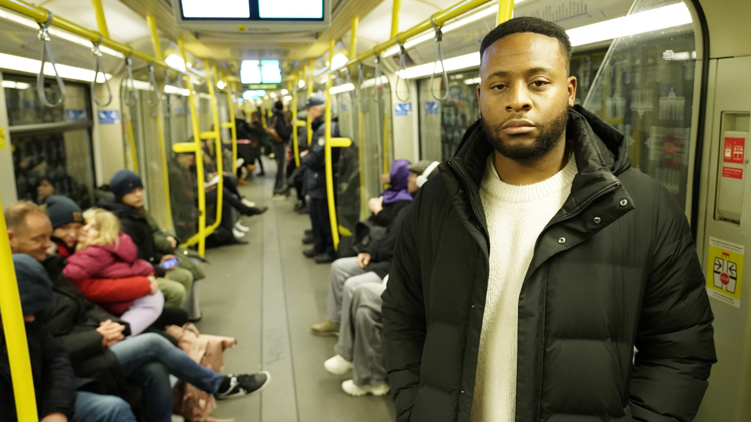"37°: Die Farbe meiner Haut - Alltagsrassismus in Deutschland": Cedric steht in der U-Bahn und schaut traurig. Im Hintergrund sitzen andere Fahrgäste.