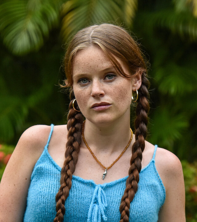 "Death in Paradise - Die Schlange": In einem Garten steht Daisy McCrae (Imogen King). Die Hände hat sie locker in die Hosentaschen gesteckt.