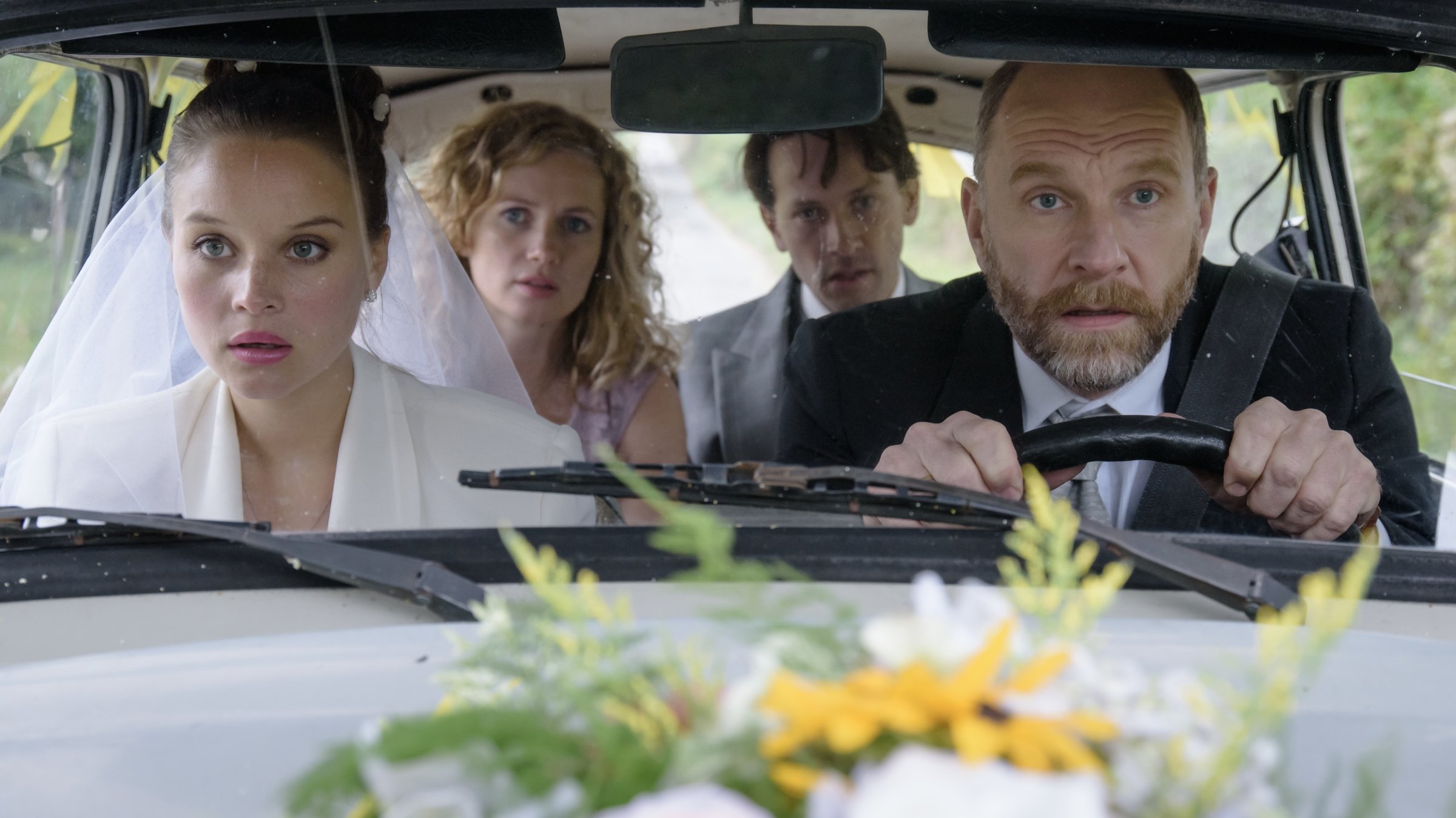 "Honigfrauen - 3. Hochzeit im Paradies": Karl (Götz Schubert) sitzt am Steuer seines Trabis, seine Tochter Maja (Sonja Gerhardt) als Braut gekleidet auf dem Beifahrersitz. Catrin (Cornelia Gröschel) und Rudi (Franz Dinda) sitzen auf der Rückbank des Trabi.