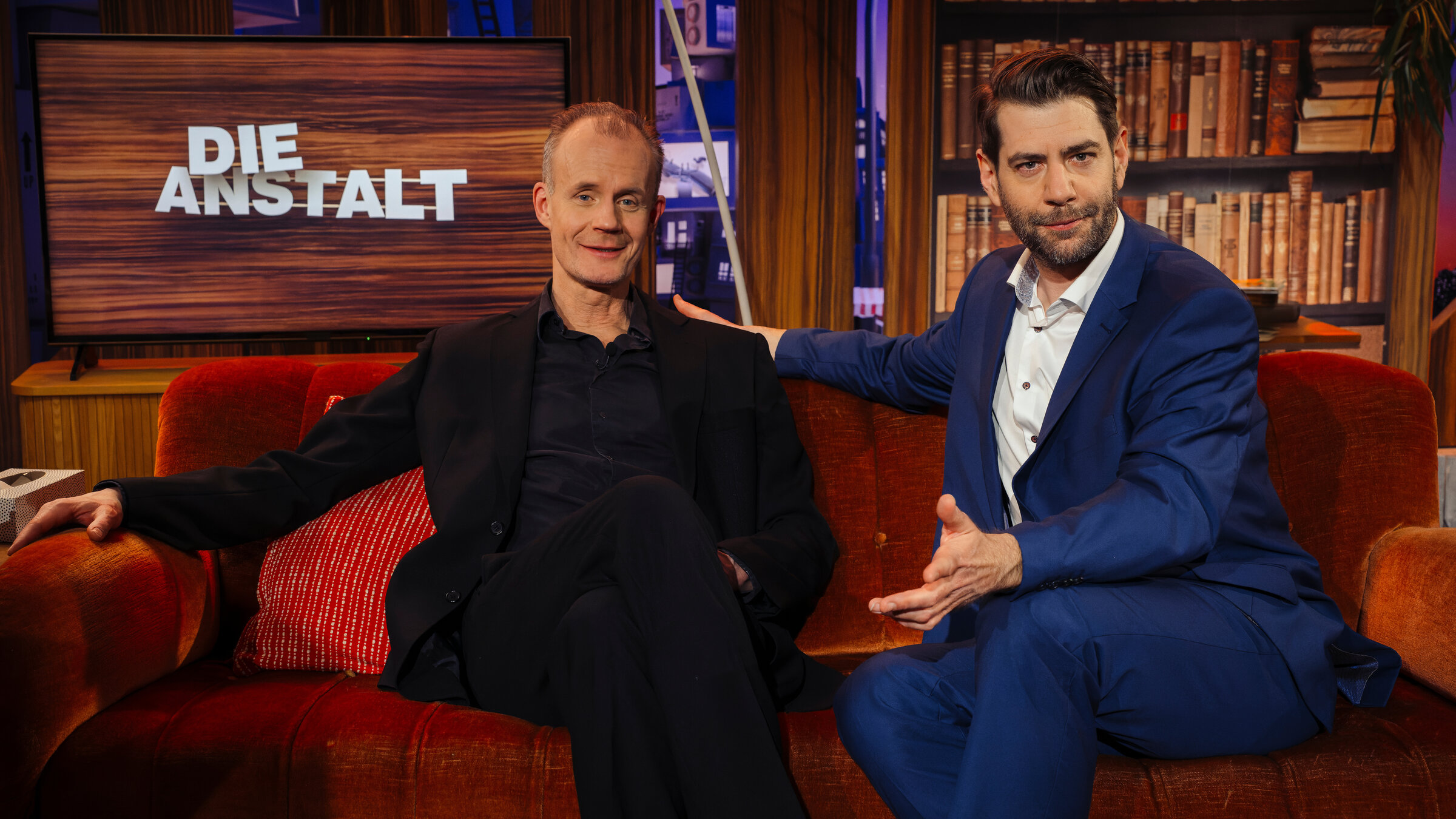 "Die Anstalt": Max Uthoff und Claus von Wagner sitzen in der Ausgabe zum zehnjährigen Jubiläum der Sendung gestikulierend vor dem Sendungslogo.