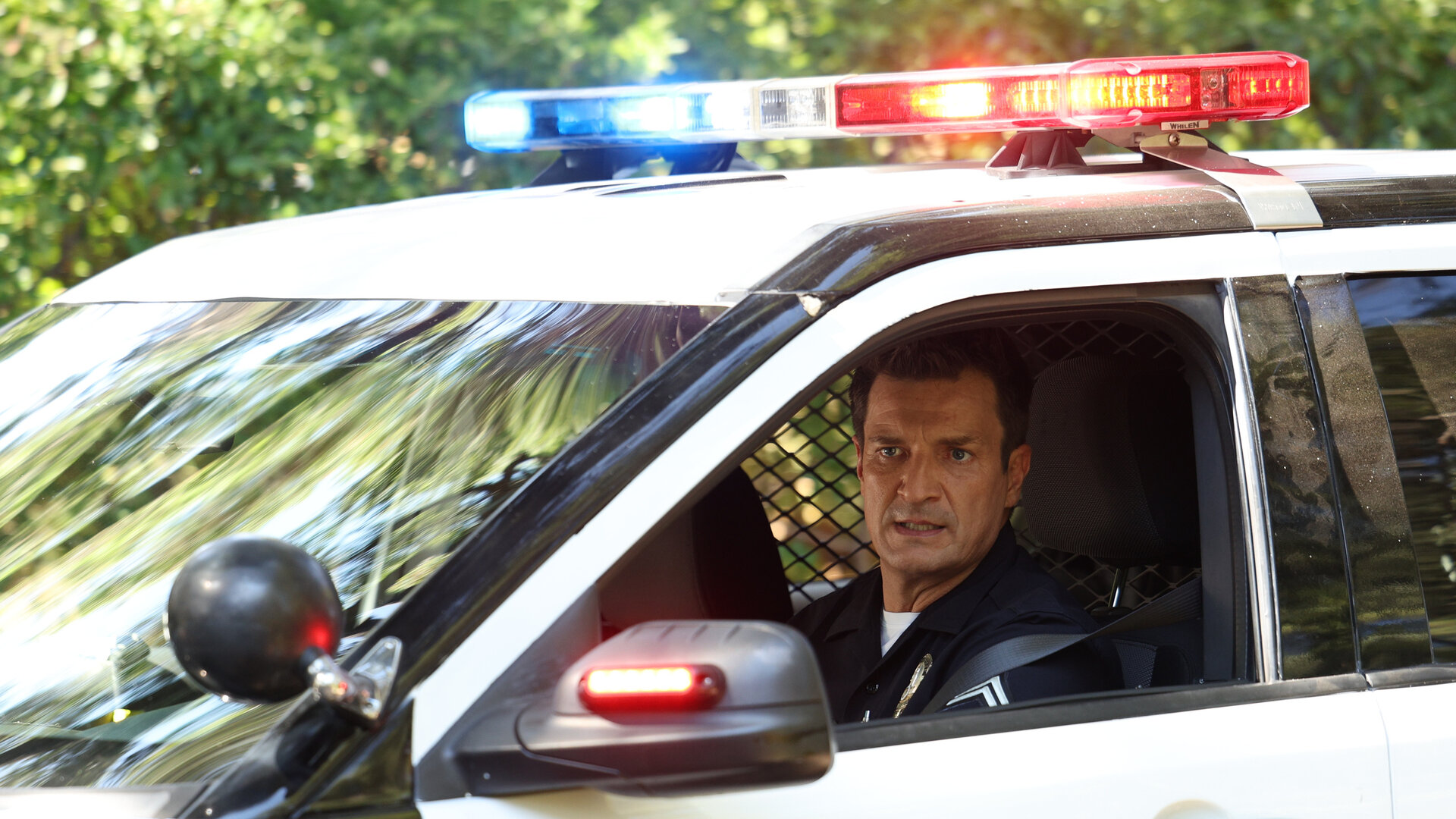 "The Rookie - Die Jäger": Officer John Nolan (Nathan Fillion) schaut aus dem Fenster eines Polizeiwagens, dessen Blaulicht hell leuchtet.