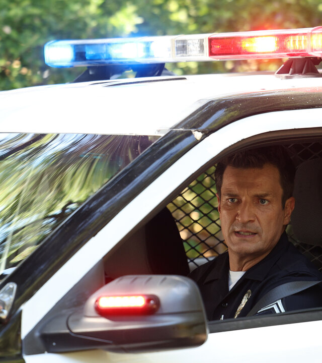 "The Rookie - Die Jäger": Officer John Nolan (Nathan Fillion) schaut aus dem Fenster eines Polizeiwagens, dessen Blaulicht hell leuchtet.
