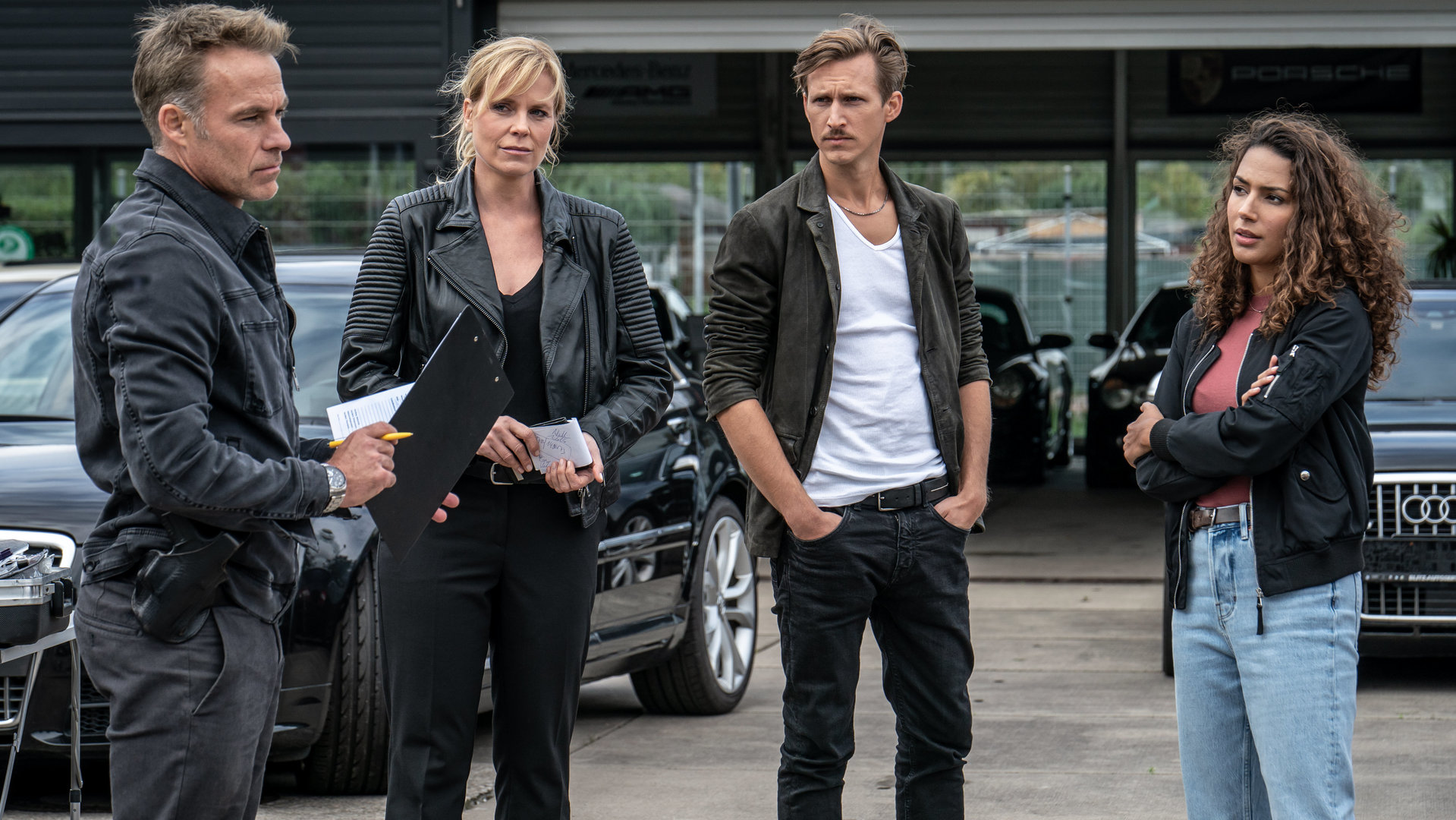 "SOKO Leipzig - Für Luise":  Jan Maybach (Marco Girnth), Ina Zimmermann (Melanie Marschke), Moritz Brenner (Johannes Hendrik Langer) und Kim Nowak (Amy Mußul) stehen vor einem Autohaus nebeneinander und besprechen sich.